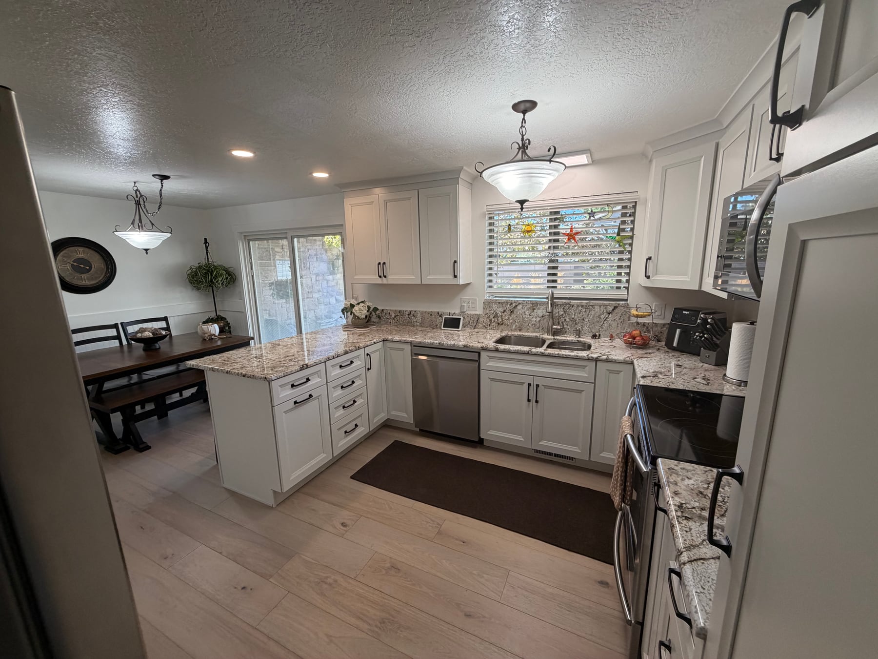 Finished kitchen sink and cabinet run with white cabinetry, black hardware, and stone counters